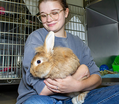 A young woman holding a rabbit outside a kennel in an animal shelter.