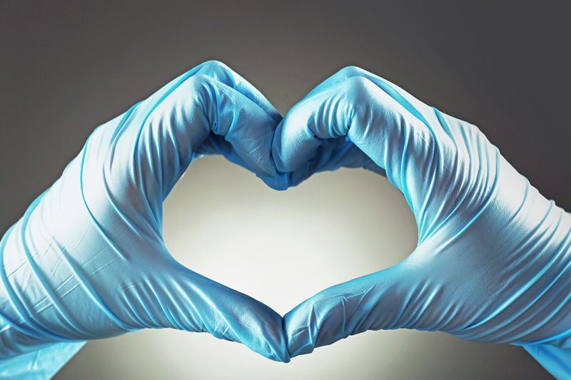 hands wearing blue latex gloves form a heart